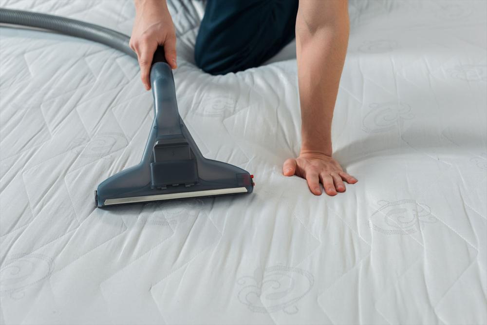 yatağın üzerinde süpürge ile temizlik yapan kişi